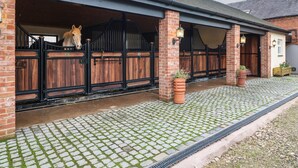 A stable with a horse visible through the open door, brick walls, and a cobblestone driveway. - Little Gem (Uttoxeter)