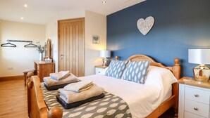 A bedroom with a wooden bed, two bedside tables with lamps, a dresser, a wardrobe, and a heart-shaped wall decoration. - Little Gem (Uttoxeter)