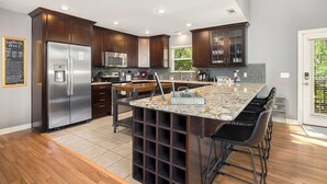 A modern kitchen with dark wood cabinets, stainless steel appliances, and a granite island with bar stools.