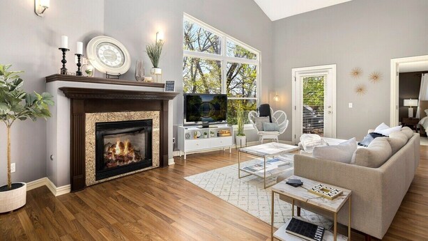 A living room with a fireplace, a television, a sofa, and a large window with a view of trees.