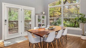A dining area with a wooden table, white chairs, and a large window with a view of trees.