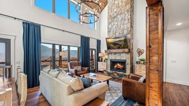 A spacious living room with a stone fireplace, a high ceiling, and a large window overlooking a scenic view.