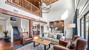 A spacious living area with a high ceiling, a staircase, and a large window.