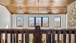 A room with a wooden ceiling, stone wall, and three windows with mountain views.