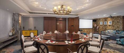 A conference room with a round table, chairs, a chandelier, a projector screen, and a sofa.
