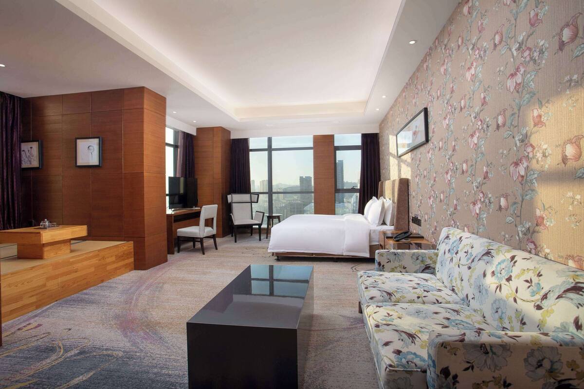 A hotel room with a bed, a sofa, a desk, and a TV.