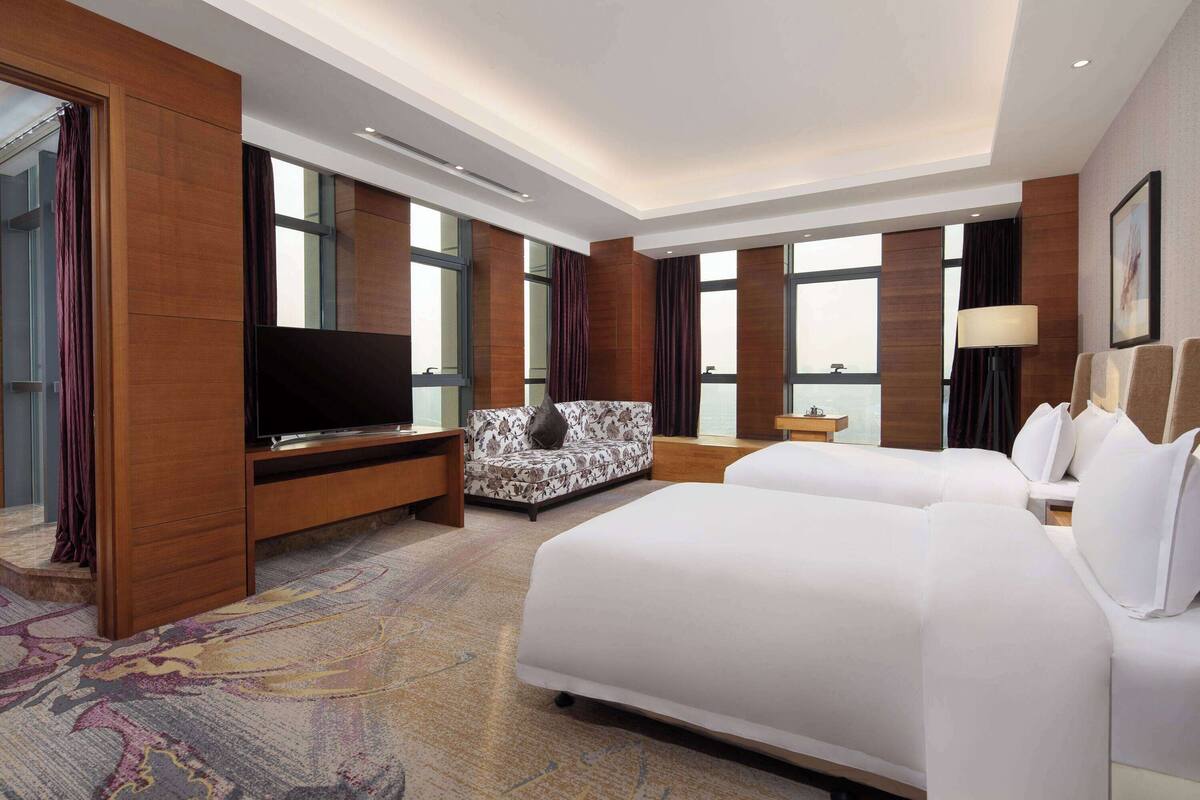 A hotel room with a large bed, a sofa, a TV, and a view of the city.