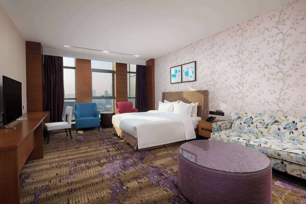 A hotel room with a large bed, a sofa, a chair, a desk, and a television.