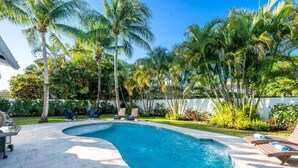 A swimming pool with lounge chairs and palm trees.