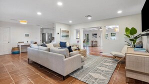 A spacious living area with a sofa, a coffee table, and a TV. There is a kitchen area in the background.