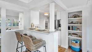 A kitchen with white cabinetry, a central island with bar stools, and a shelving unit with decorative items.