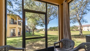 A room with large windows, a view of a courtyard with trees and buildings, and two white plastic chairs. - Budget Friendly Regal Palms Townhome near to Theme Parks (Davenport)