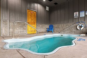 Piscina interna com uma porta de madeira, uma cadeira azul e um aviso de proibição de saltos.