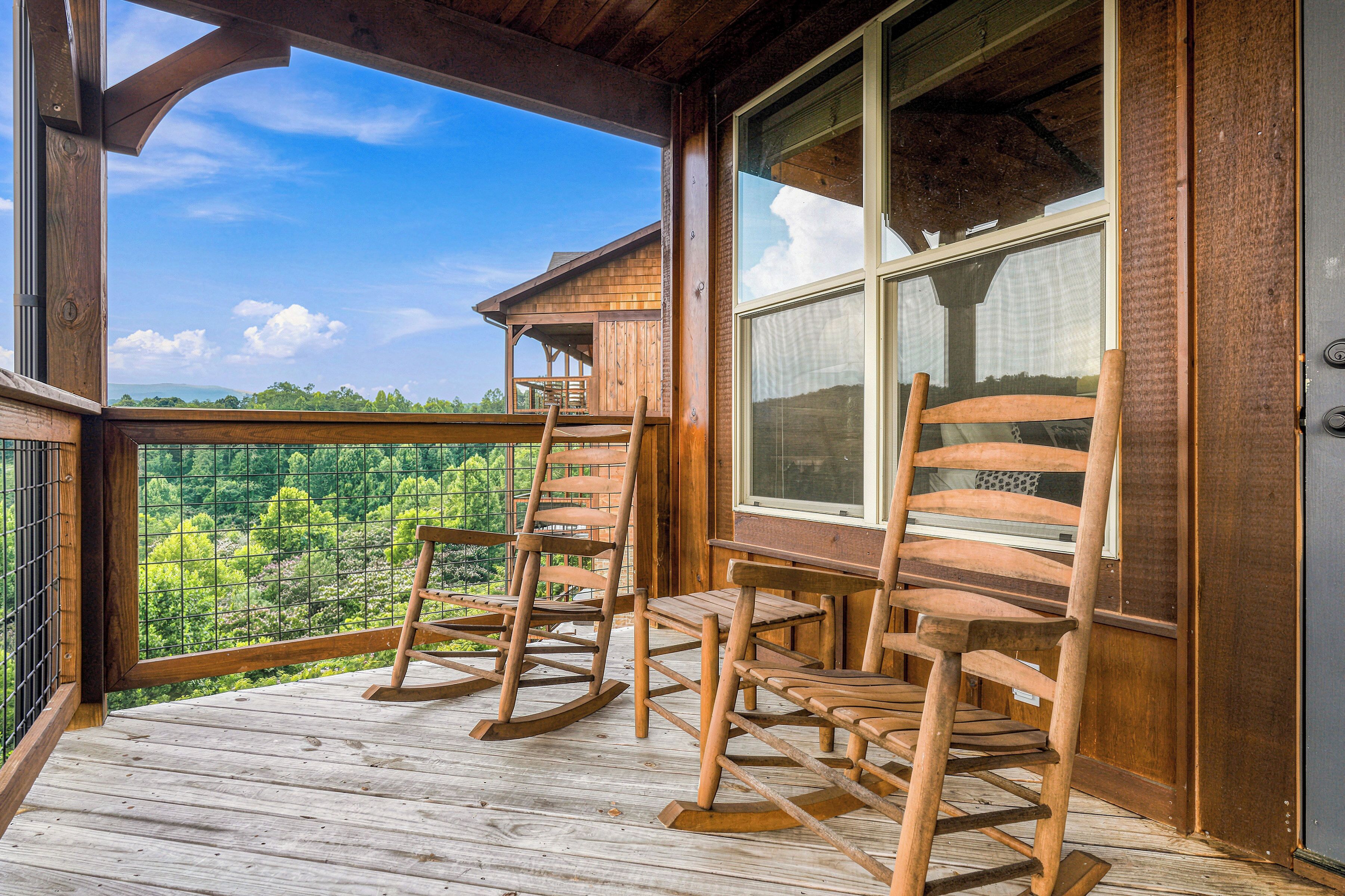 A wooden deck with rocking chairs, a large window, and a view of the forest.
