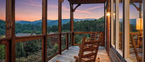 Una terraza de madera con sillas, con vistas a un paisaje boscoso y montañas a lo lejos.