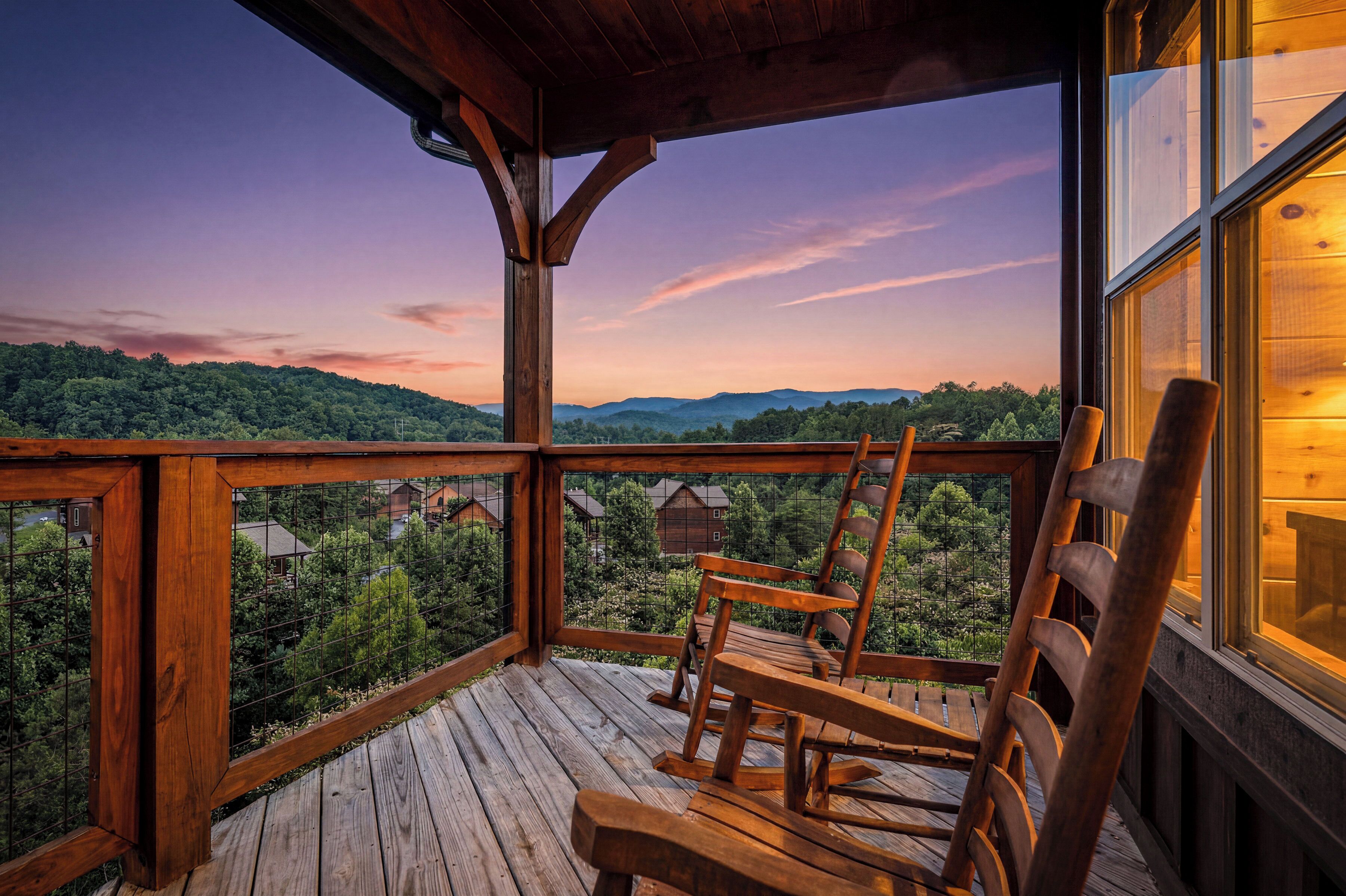 A wooden deck with a view of a forested landscape and distant mountains.