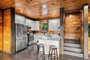 A modern kitchen with wooden walls, stainless steel appliances, and a central island with stools.