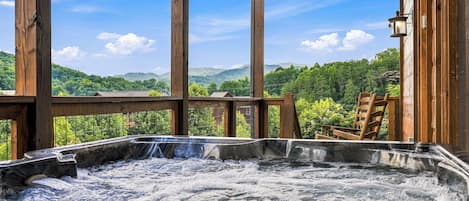 Un jacuzzi con terraza de madera y vista a un paisaje boscoso.