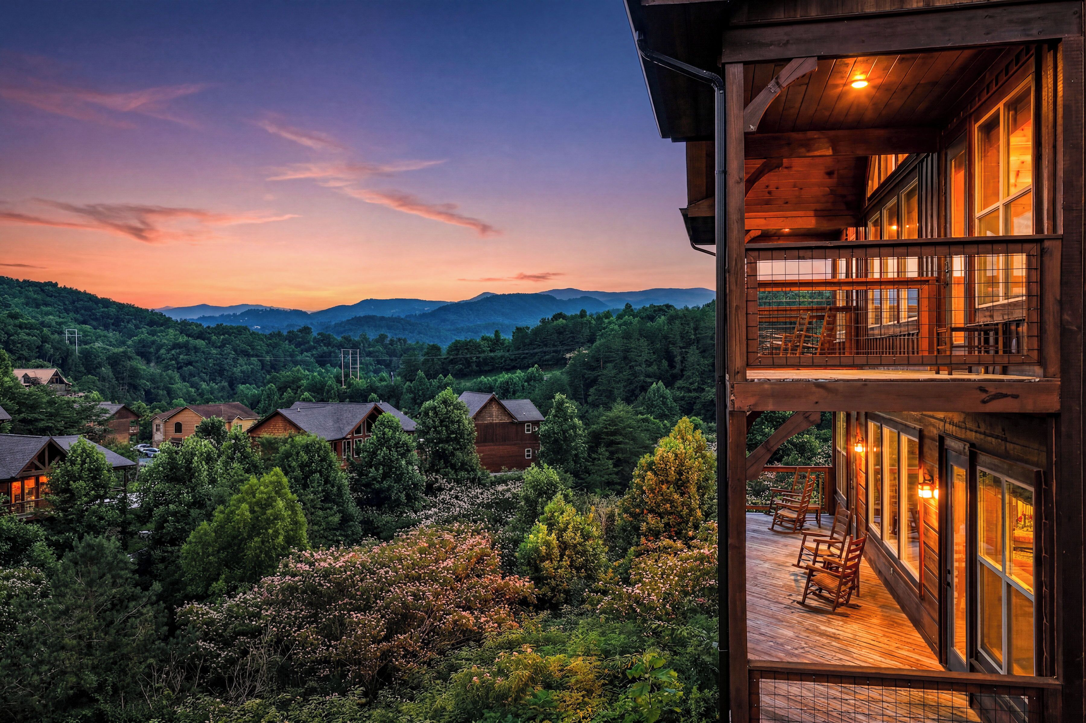 A multi-story building with a balcony overlooking a forested valley and distant mountains.