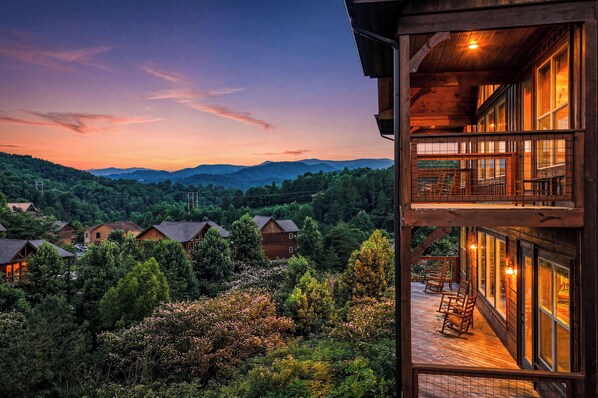A multi-story building with a balcony overlooking a forested valley and distant mountains.