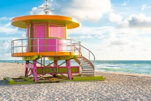 Ein Rettungsturm mit einer Wendeltreppe, auf einem sandigen Strand mit dem Meer im Hintergrund.