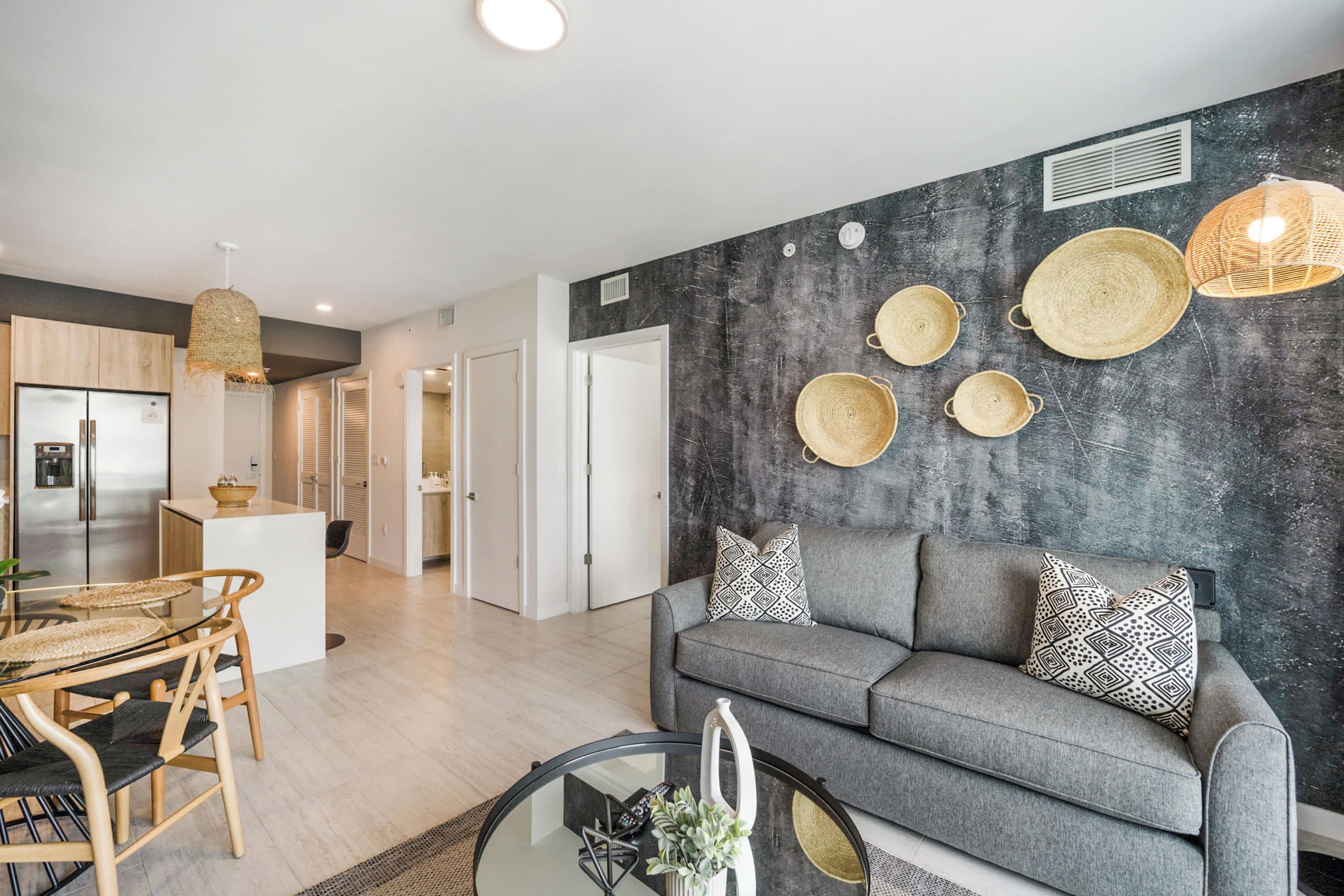 A modern living room with a grey sofa, a glass coffee table, and a dining area with a wooden table and chairs.