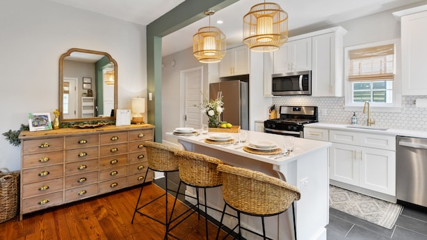 A modern kitchen with white cabinetry, a central island with bar stools, a large mirror, and pendant lighting. - The Charleston Suites: The Emerson Suite (Charleston)