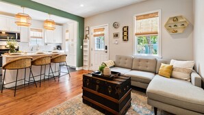 A modern kitchen with white cabinets, a dining area with bar stools, a sofa, and a coffee table with a vintage suitcase. - The Charleston Suites: The Emerson Suite (Charleston)
