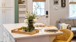 A kitchen with a central island, white cabinetry, and a wicker chair. - The Charleston Suites: The Emerson Suite (Charleston)