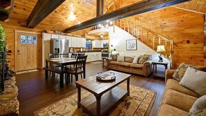 A spacious living area with a wooden ceiling, a dining table, a sofa, and a staircase leading to a kitchen. - The Busy Beaver Lodge (McCurtain County)