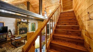 A wooden interior with a fireplace, a TV, and a staircase. - The Busy Beaver Lodge (McCurtain County)