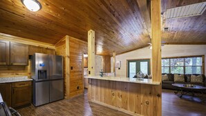 L’intérieur d’une cabane en bois comprend un coin cuisine équipé d’un réfrigérateur en acier inoxydable, de meubles de rangement en bois et d’un comptoir en bois.