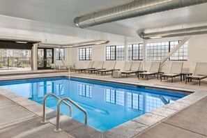 Una piscina interior con agua cristalina, sillas de descanso y amplias ventanas.