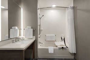 Un baño moderno con ducha curva, espejo grande y tocador con dos lavamanos.