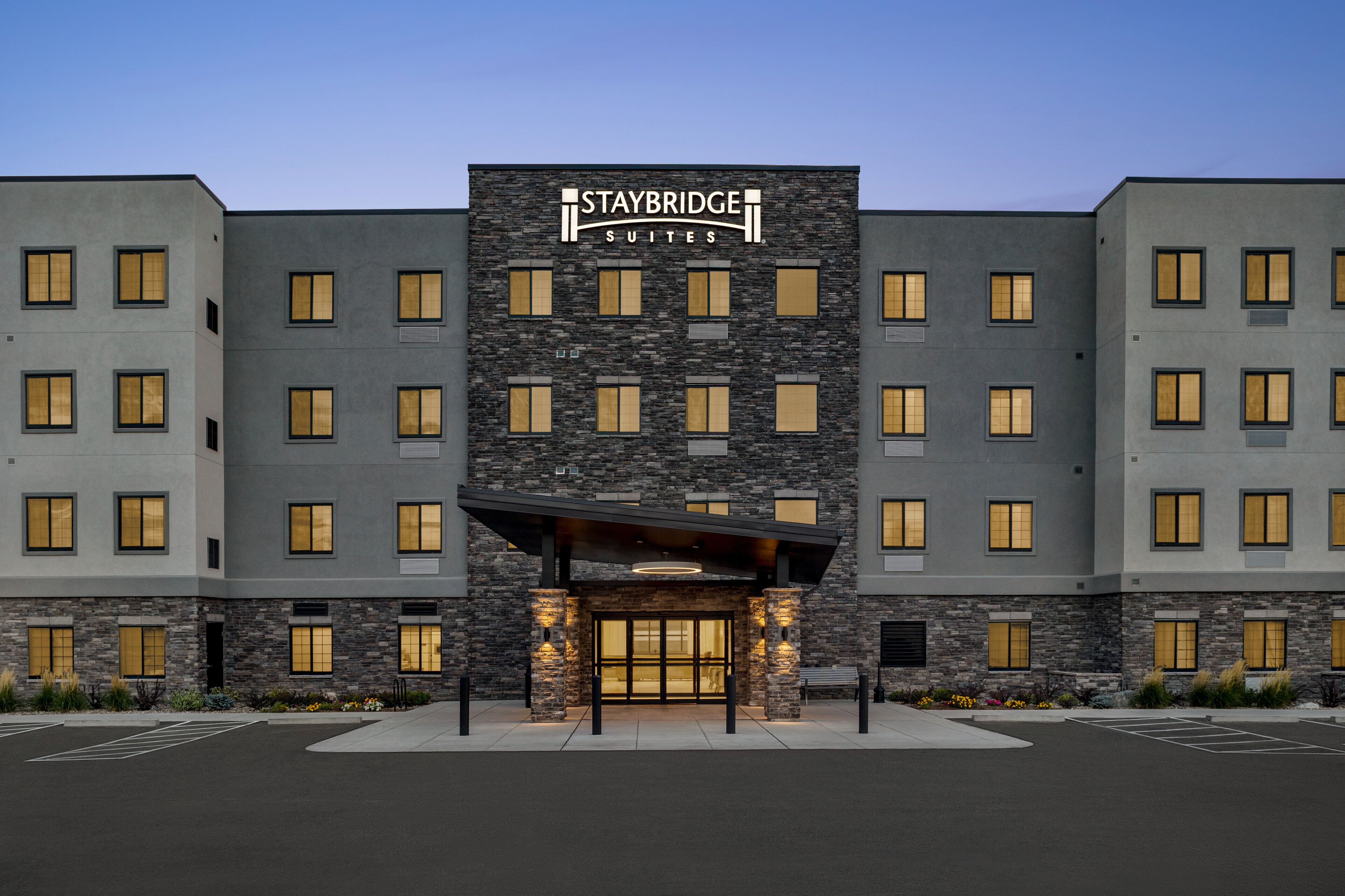 Un hotel Staybridge Suites con un diseño moderno, que cuenta con fachada de piedra y varias ventanas.