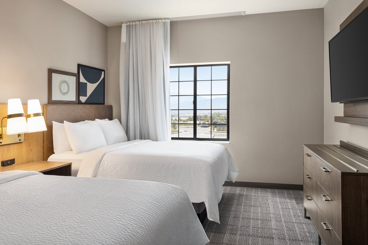 Habitación de hotel con dos camas, un ventanal con vistas, un televisor de pantalla plana y un aparador de madera.