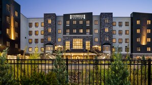 Um hotel Staybridge Suites com design moderno, com vários andares e uma entrada destacada com escadaria.