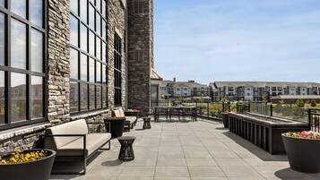 A rooftop terrace with stone walls, large windows, outdoor seating, and a view of other buildings.