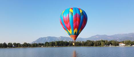 A hot air balloon over a calm lake with a clear sky and mountains in the background.