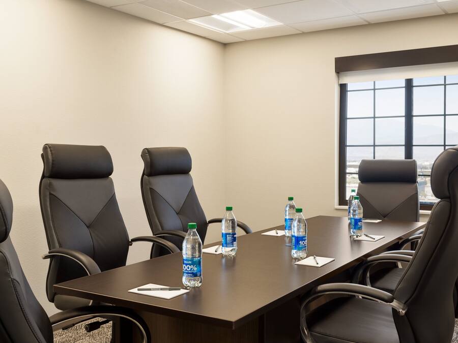 Uma sala de conferências com uma mesa comprida, seis cadeiras de couro preto e garrafas de água sobre a mesa.