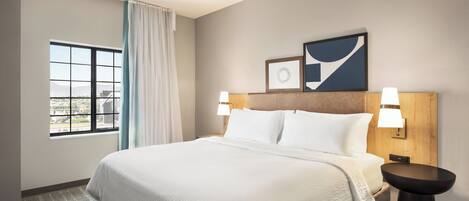 A hotel room with a large bed, a window with a view, a bedside table, and wall-mounted lamps.