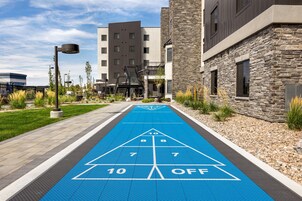 Una cancha de shuffleboard azul con los números 10, 8, 7 y la palabra 'OFF' visibles, rodeada de edificios y un farol.