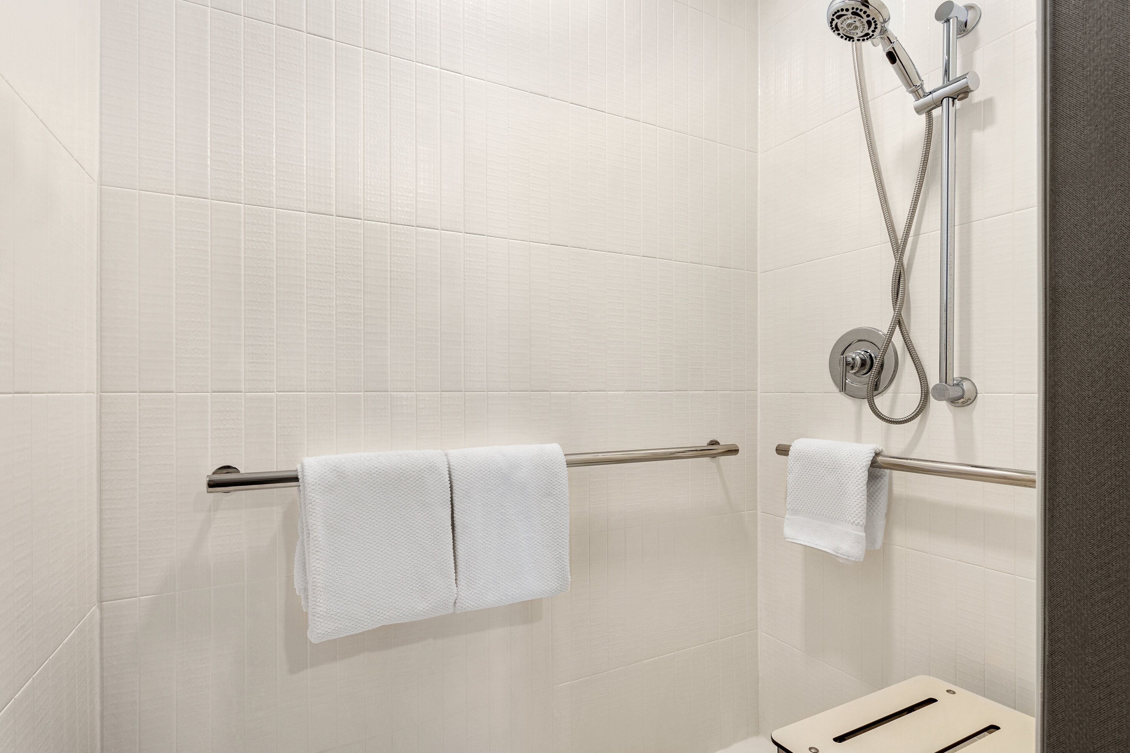 A shower area with white tiles, a towel rack with two towels, and a showerhead.