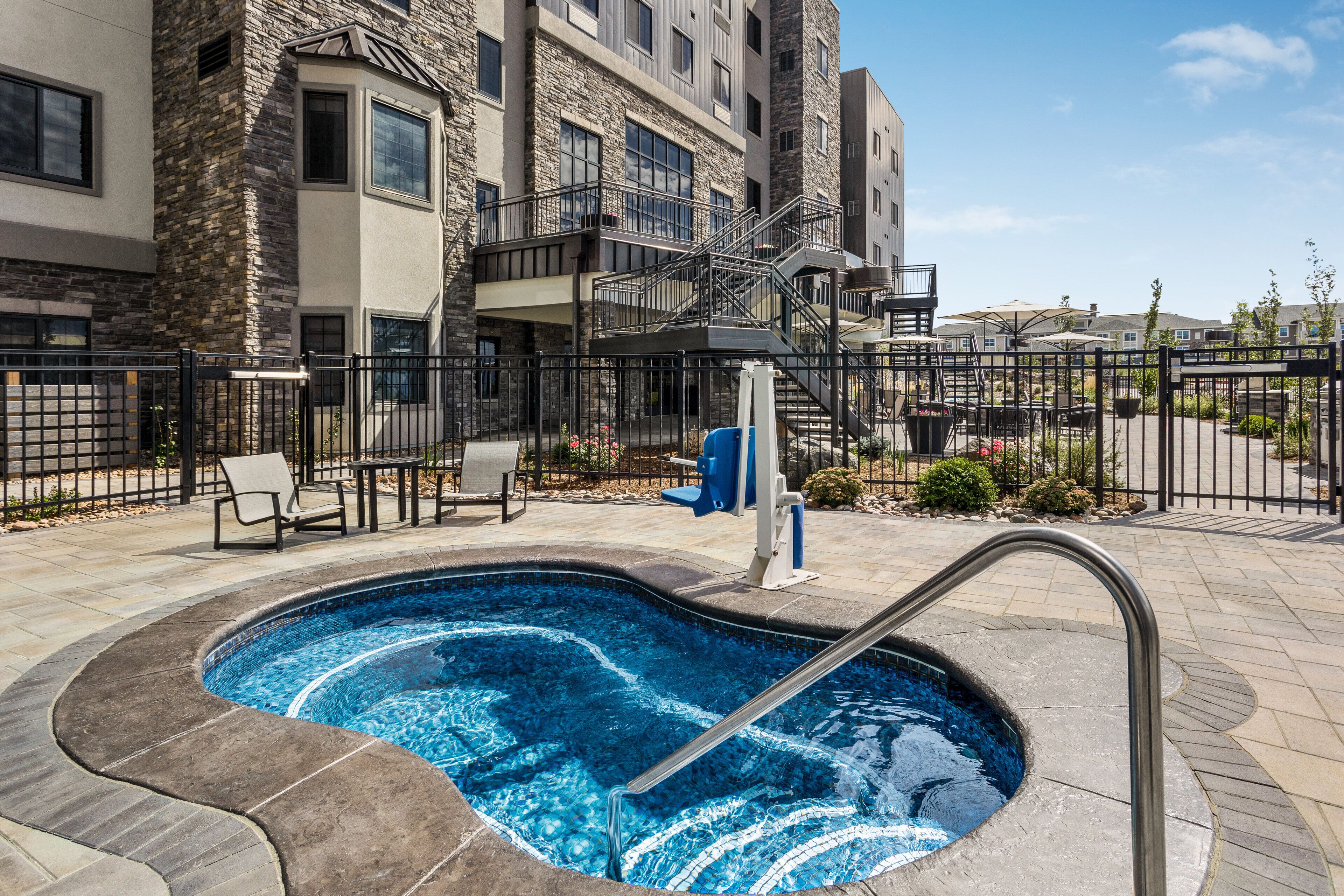 A swimming pool with a metal ladder, surrounded by a stone deck and a black fence.