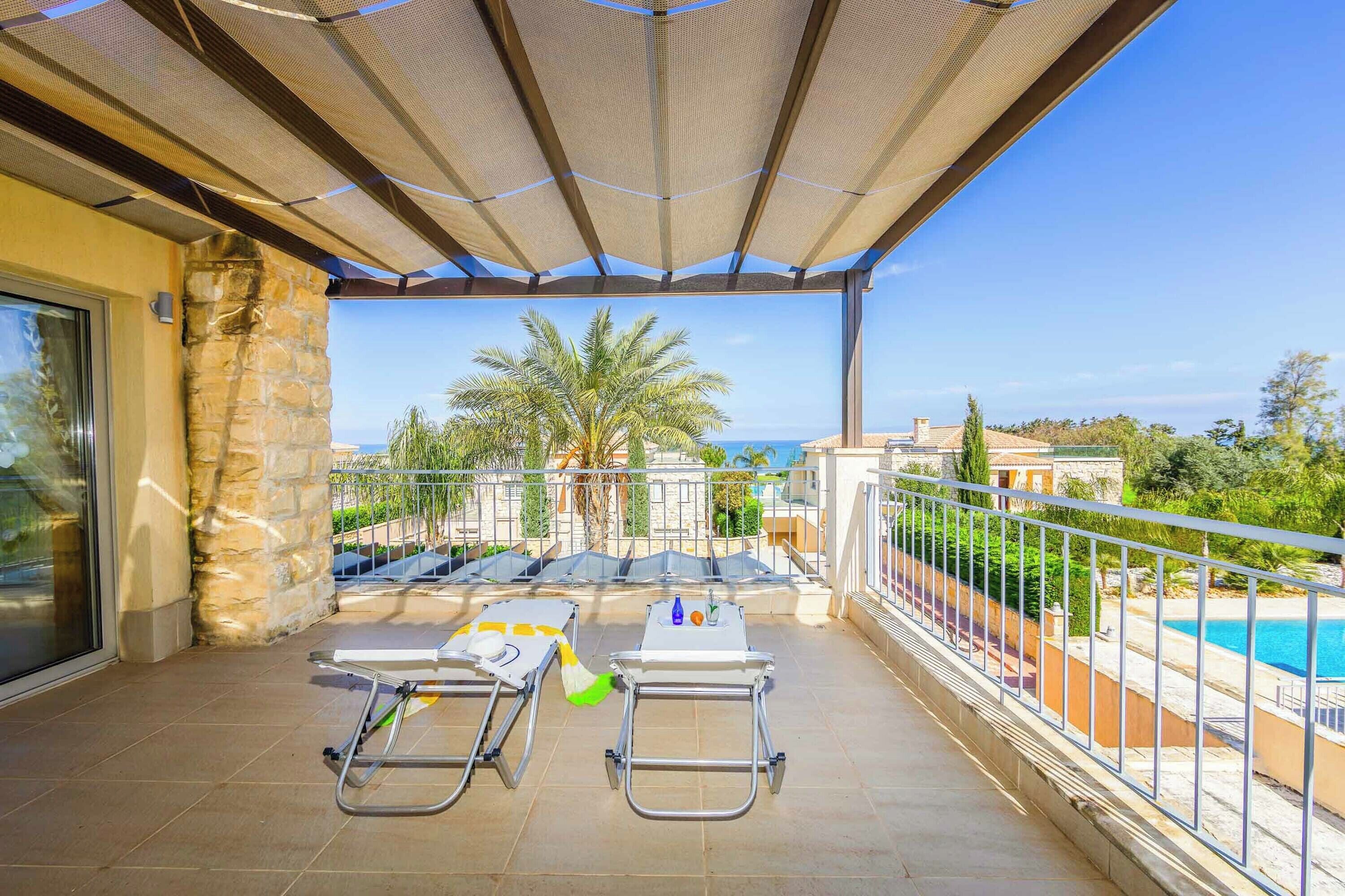 A covered outdoor area with a pool, lounge chairs, and a view of the sea.