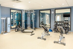 A gym with exercise equipment, mirrors, and a weight rack.