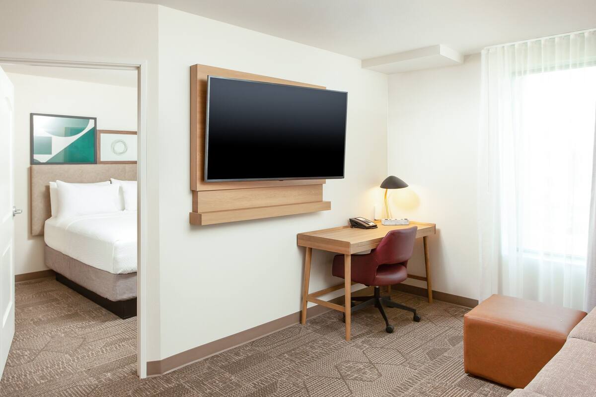 A hotel room with a bed, a desk with a chair, a television, and a window with curtains.