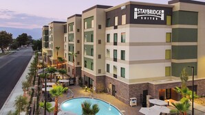 Un hotel Staybridge Suites con área de piscina, mobiliario exterior y vista a la calle.