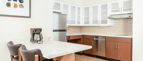 Una cocina moderna con armarios blancos, un refrigerador de acero inoxidable, una cafetera y un comedor con sillas.