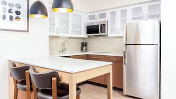 A modern kitchen with white cabinets, a stainless steel refrigerator, a microwave, and a wooden dining table with chairs.